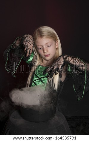 girl dressed as Halloween witch with cauldron isolated on dark background