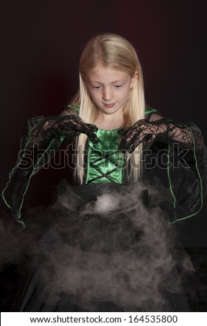 girl dressed as Halloween witch with cauldron isolated on dark background