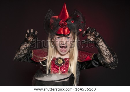 girl dressed as Halloween witch with cauldron isolated on dark red background
