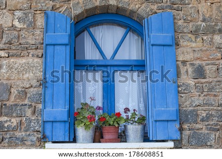 decorative window with blue painted shutters and red geraniums in pots  in Elounda, Crete