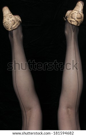 Vintage 1940 style woman in seamed stockings with her legs in the air, isolated on black background