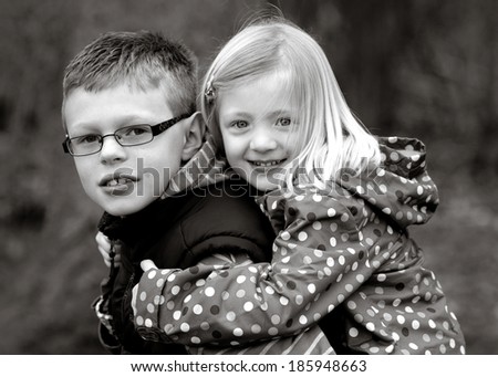 pretty child having a piggy back on her brother\'s back in black and white