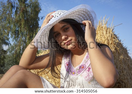 Adolescents in the hay bale at the end of summer. Young girl in the field enjoying a summer afternoon. Brunette with hat on the field in the straw.