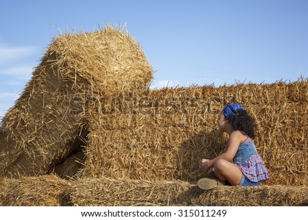 Little girl in the hay bale at the end of summer. Young girl in the field enjoying a summer afternoon.
