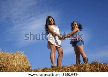 Little teenage girl in the hay bale at the end of summer. Two sisters enjoying the countryside a summer afternoon.