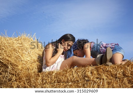 Little teenage girl in the hay bale at the end of summer. Two sisters enjoying the countryside a summer afternoon.