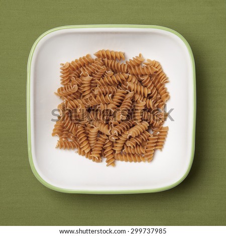 Dried whole wheat pasta in white bowl, green background