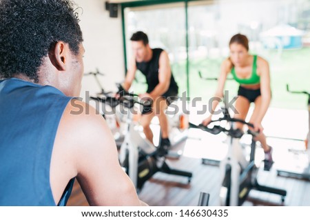 Two men and a woman are on fitness bicycles at a fitness center
