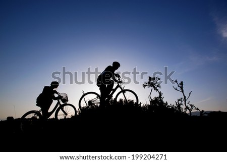 Silhouette of a man and girl on mountain bike at sunset
