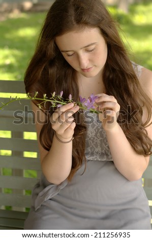 Teen aged girl looking down at spring of purple blossoms on a porch swing in summer wearing gray dress with lace