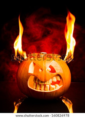 Evil face of Halloween pumpkin with flames and red smoke in the background.