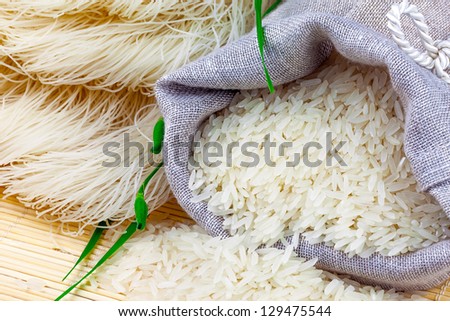 Macro view of sack with white rice and rice vermicelli with greens on the mat