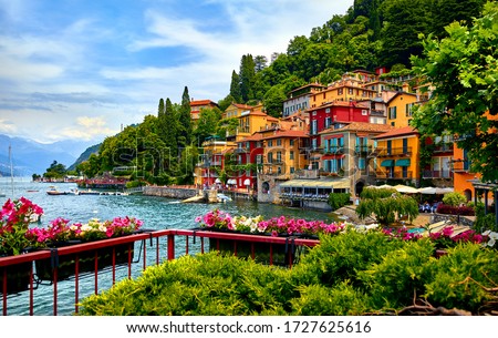Varenna, Italy. Picturesque town at lake Como. Colourful motley Mediterranean houses at stone beach coastline among green trees. Popular health resort and touristic location. Summer day landscape.