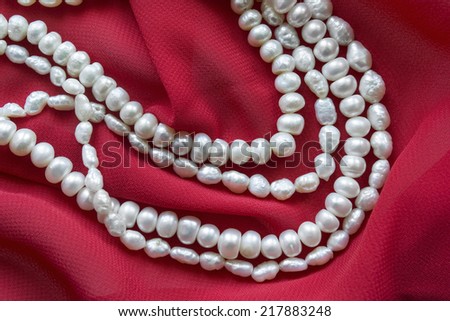 Strings of white pearl on draped red silk as a background