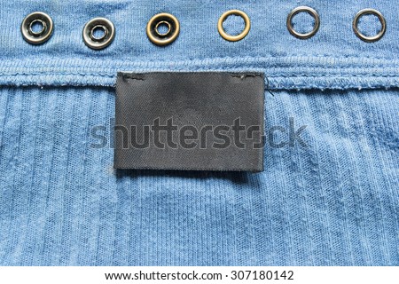 Blank black clothes label on blue cloth as a background