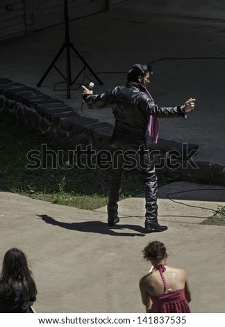 LAKE GEORGE, NEW YORK - JUNE 1: An Elvis Presley look-a-like in a leather jacket  performs before a group of people on June 1, 2013 in Lake George, New York.