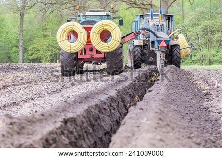Two agriculture tractors digging drainage pipes in ground