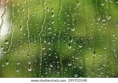 Rain drops on window with green tree in background , spring rainy day