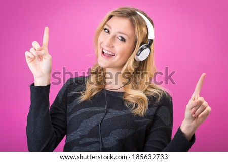 Young beautiful woman in bright outfit enjoying the music with her headphones. Studio portrait on pink background
