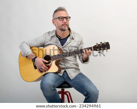 Closeup of young man with black glasses practicing and playng guitar. Studio portrait in gray background