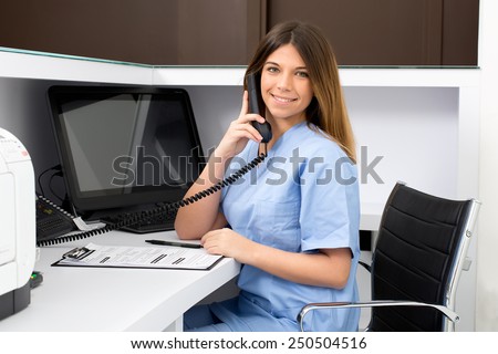 Portrait of a beautiful smiling nurse at desk station while talking on the phone and complete a medical information form