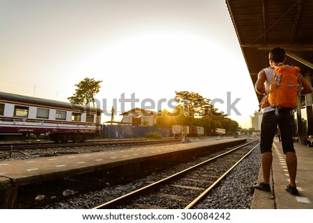 Backpacker with orange bag waiting a train at platform.