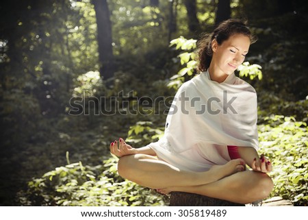 Woman practicing yoga in deep forest. Sitting on wooden log/Woman in lotus position practicing mudra meditation Young woman in lotus position practicing