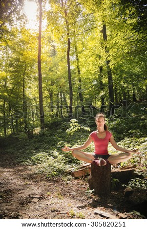 Woman practicing yoga in deep forest. Sitting on wooden log/Woman in lotus position practicing mudra meditation Young woman in lotus position