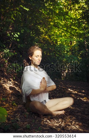 Young woman practicing yoga in woodland. Beautiful fit woman in white cloth practicing yoga in deep green forest/Young fit woman meditating in nature