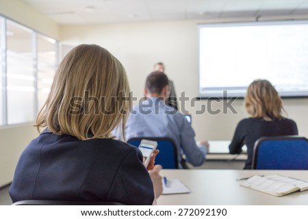 people sitting rear at the desks in the education class. close up rear view of the woman watching her mobile