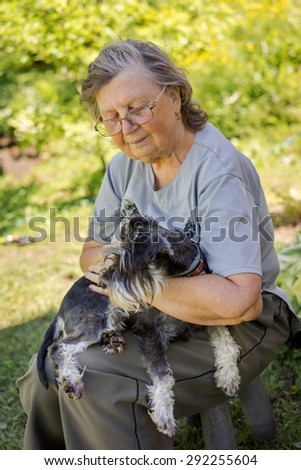 Senior woman hugs her black and silver miniature schnauzer dog in countryside