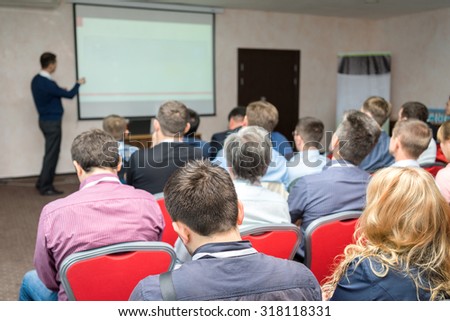 conference audience: people sitting rear at the business training and lecturer near the whiteboard pointing at the screen