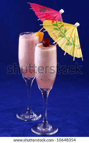 Two pineapple, cherry smoothies with umbrellas on blue background