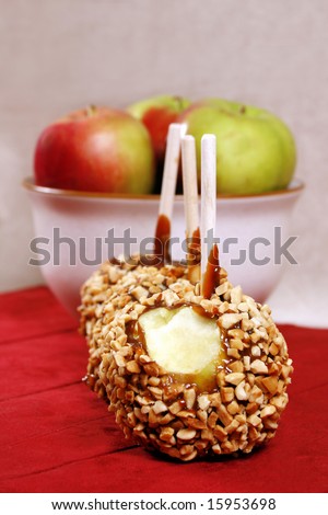 caramel and nut covered apple with another bowl of apples behind it.  Shallow depth of field with focus on foreground apple