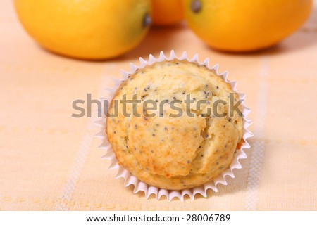 single lemon poppy seed muffin with lemons in the background on a yellow placemat