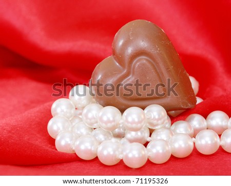 chocolate heart resting on a string of pearls with red satin in the background in a vertical format.  Could be used for Valentine, anniversary or romantic