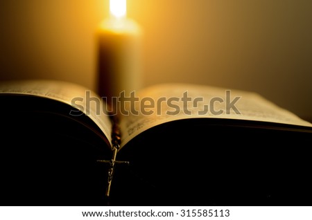 Opened book with rosary in front of the blurred burning candle. Shallow DOF. Imagine de stoc © 