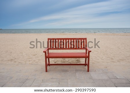 Alone wooden red beach chair sitting on the sand with sea.