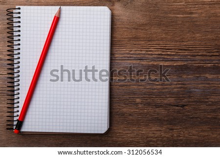 Empty notepad on wooden surface and red pencil