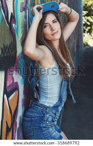 Young girl in denim overalls posing against wall with graffiti