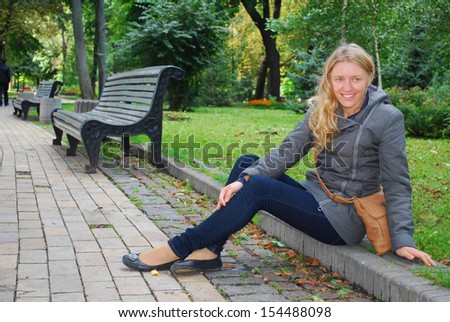 In autumn park, girl sitting on the curb
