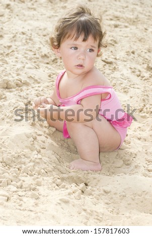 In the summer, on the beach in the sand little girl sits and plays