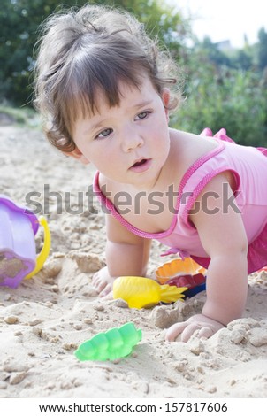 In the summer, on the beach in the sand little girl sits and plays with a bucket