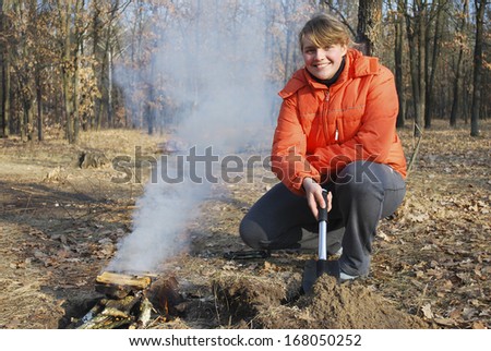 At a picnic, in the autumn forest, bright sunny day girl kindles a fire and holding a shovel, fire smokes heavily