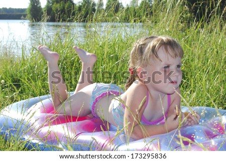 Summer little girl sunning at the lake in the grass, it lies on an inflatable mattress.