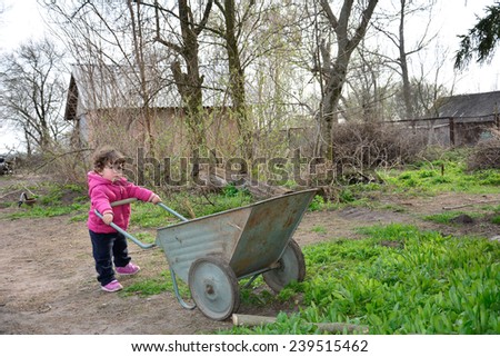 Spring dirty little rural  girl carries a wheelbarrow.