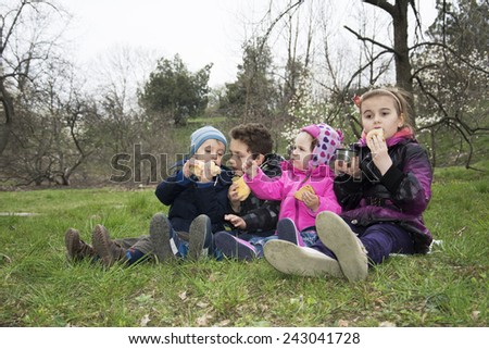 In the spring of four small child sitting in the meadow on the grass and eat cookies.