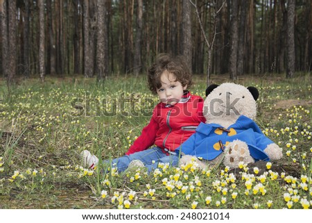 In the spring of a little girl with a bear in the woods sitting on a flower meadow.