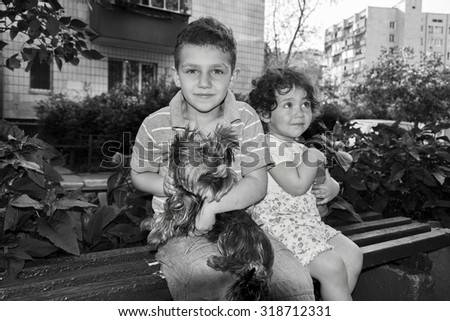 Little curly boy and a girl sitting on a bench and holding a dog in her arms. Black and white photo.