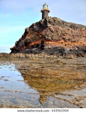 Lighthouse and cliff reflected in the water puddles, on the reef in low tide, tip of Jandia, Fuerteventura, Canary islands, Spain